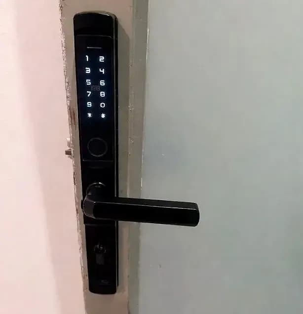A black keypad and fingerprint smart lock with a lever, fitted to a white door
